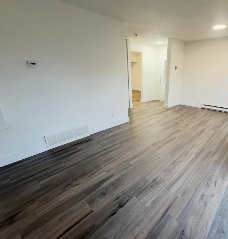 Empty renovated living room with freshly painted white walls, new baseboards and grey-brown laminate flooring