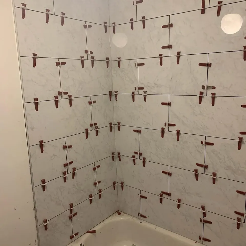 Bathtub surround being tiled with large marble-look tiles and red tile-levelling clips in place